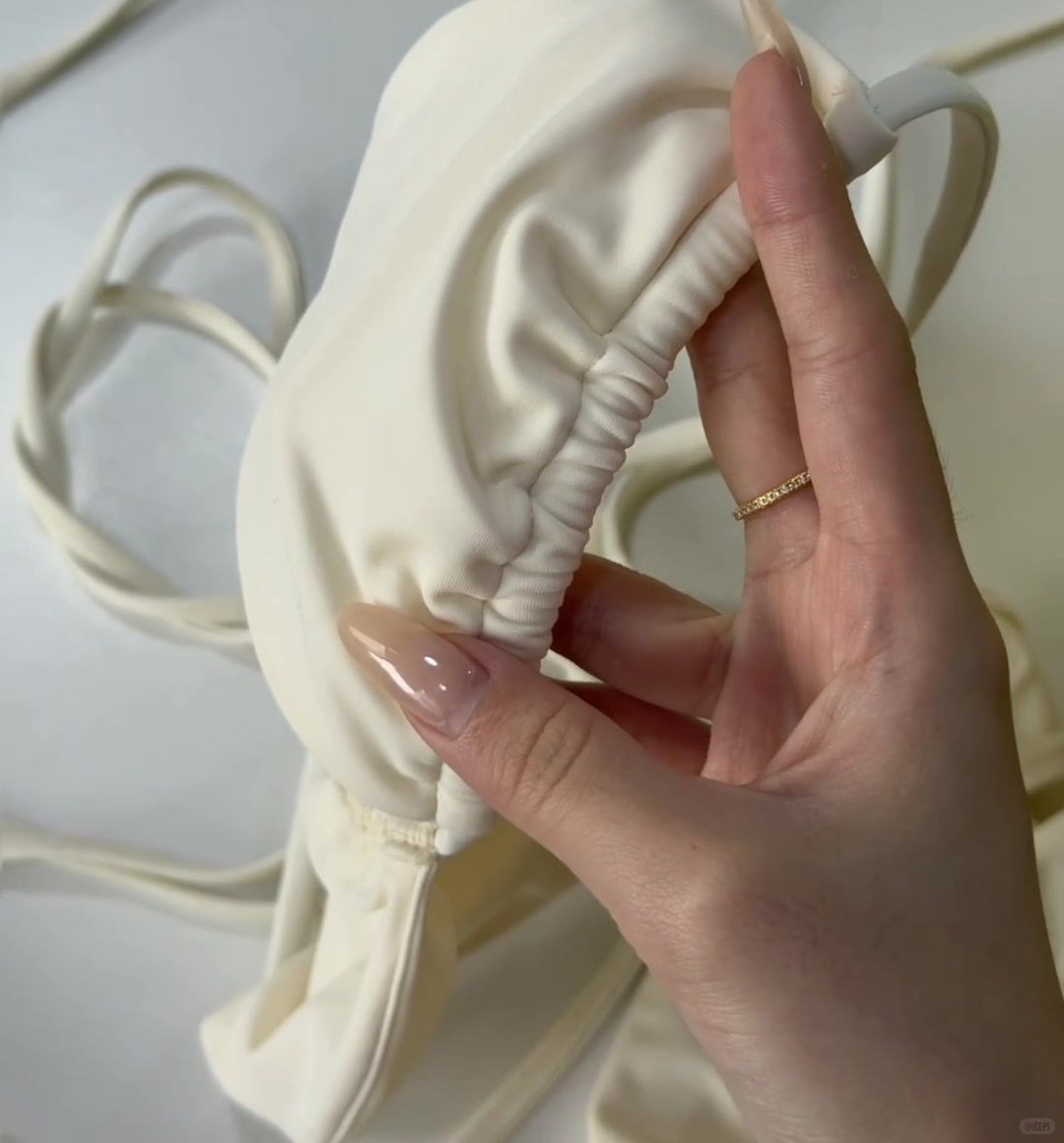 Hands holding a white gathered garment edge showing its seam finish