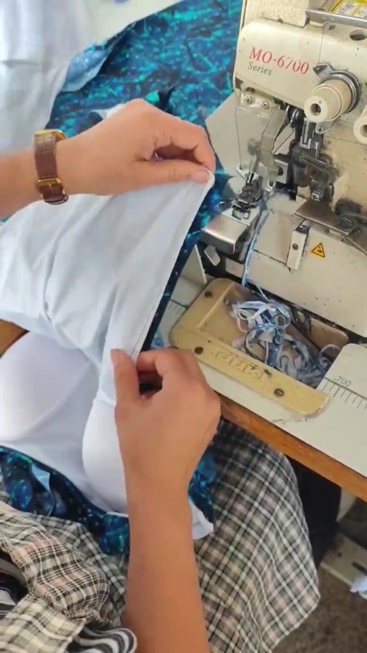 Hands aligning white lining and printed outer fabric beside a sewing machine