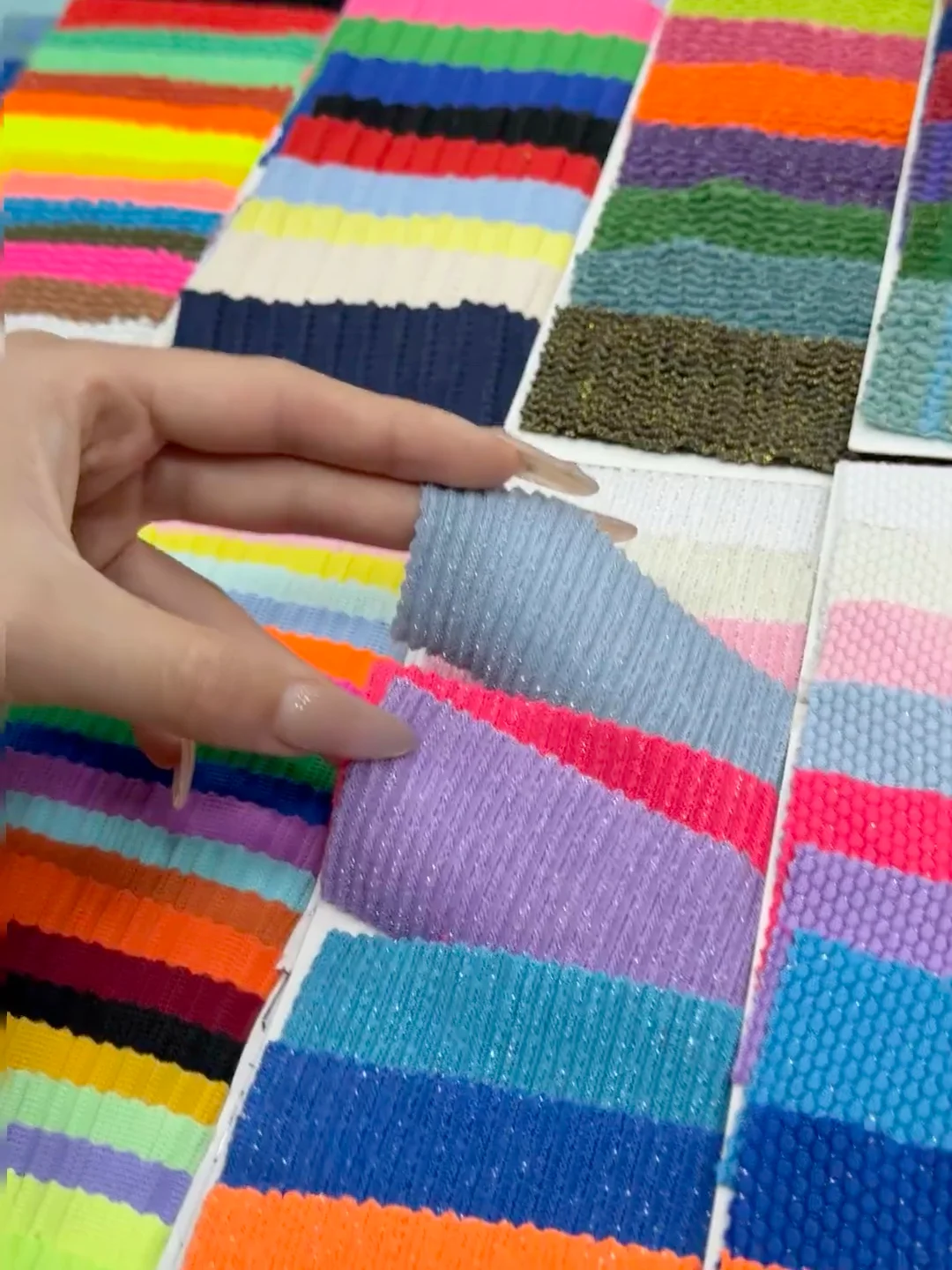 Hands comparing small knitted fabric swatches in several colors